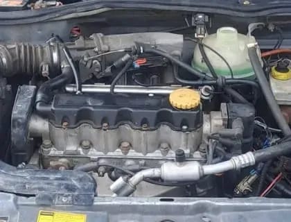 Detalle ampliado del motor del Chevrolet Chevy: tapa del motor, mangueras y depósito del refrigerante.