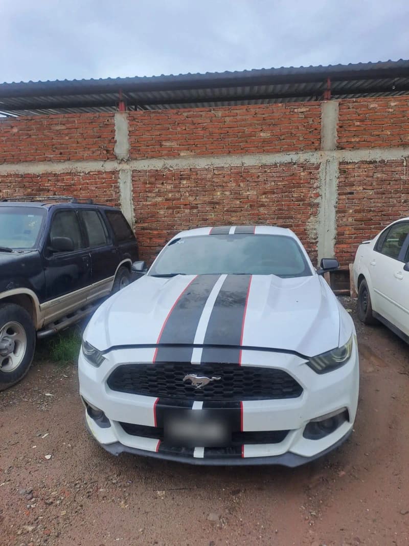 Ford Mustang blanco con franjas negras en el patio del taller.